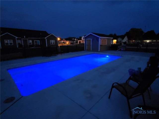 pool at twilight featuring a fenced in pool, an outdoor structure, a patio area, and a fenced backyard