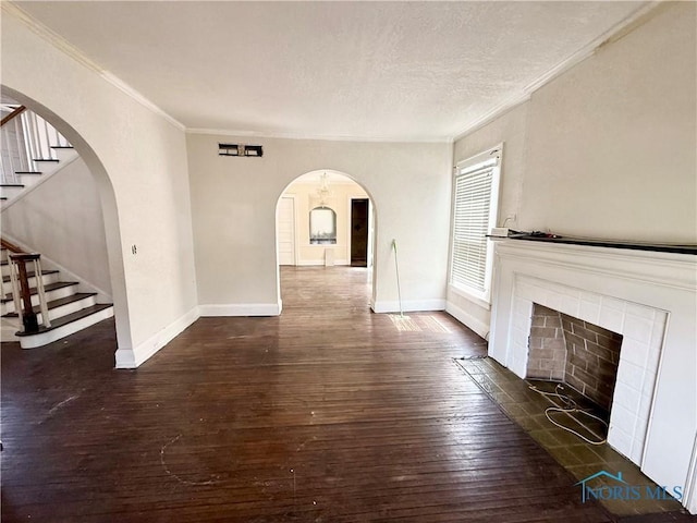 unfurnished living room with dark wood-style flooring, stairway, crown molding, baseboards, and arched walkways