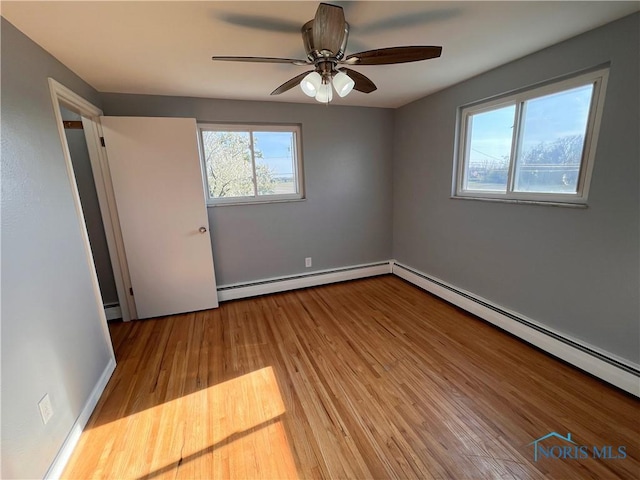 unfurnished room with a ceiling fan, baseboard heating, and wood finished floors