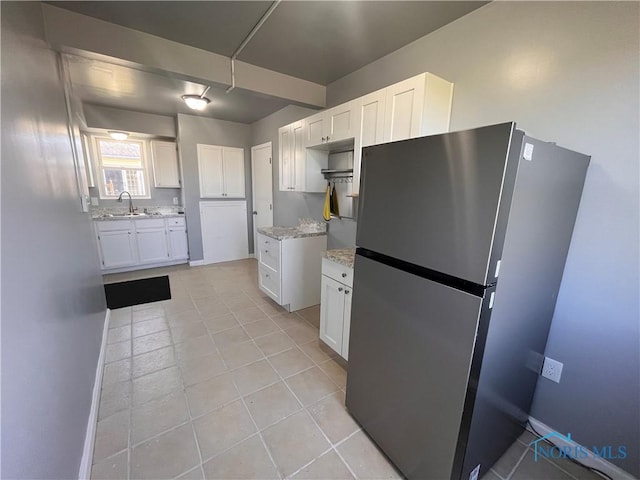 kitchen with light stone counters, freestanding refrigerator, light tile patterned floors, white cabinets, and a sink