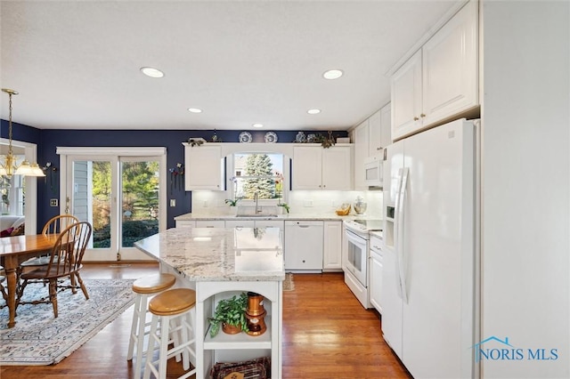 kitchen with white appliances, a kitchen island, a sink, white cabinetry, and light wood-type flooring