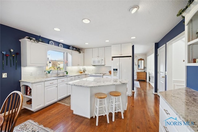 kitchen with open shelves, white cabinets, a sink, a center island, and white appliances