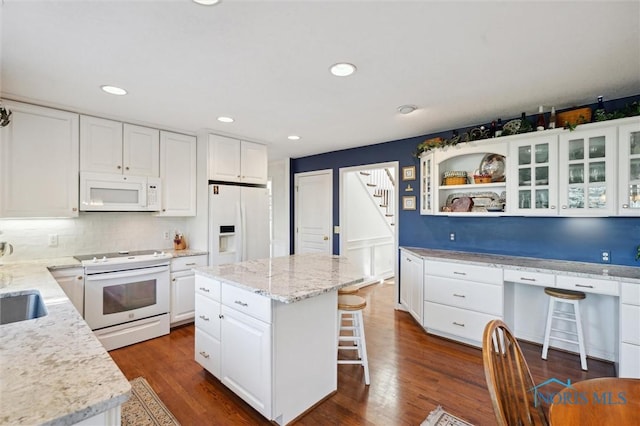 kitchen featuring glass insert cabinets, a kitchen bar, a kitchen island, white appliances, and white cabinets