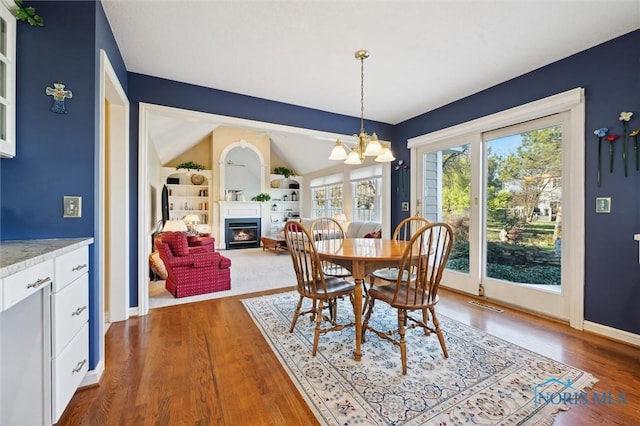 dining space with wood finished floors, an inviting chandelier, a glass covered fireplace, baseboards, and visible vents