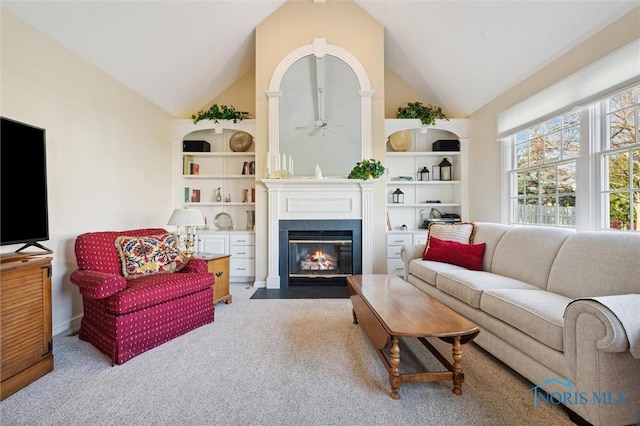living area with a ceiling fan, a fireplace with flush hearth, vaulted ceiling, and carpet