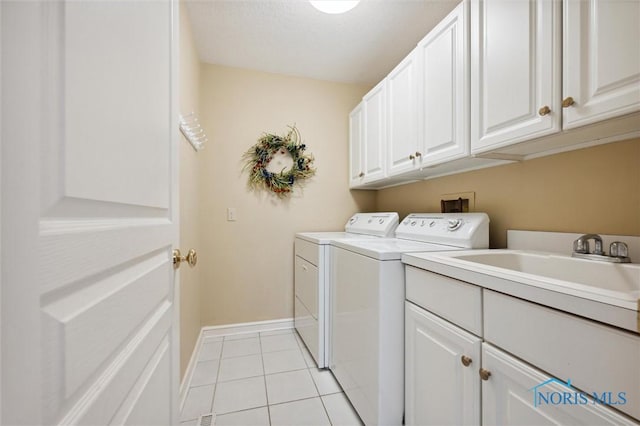 laundry room with light tile patterned floors, separate washer and dryer, cabinet space, and baseboards
