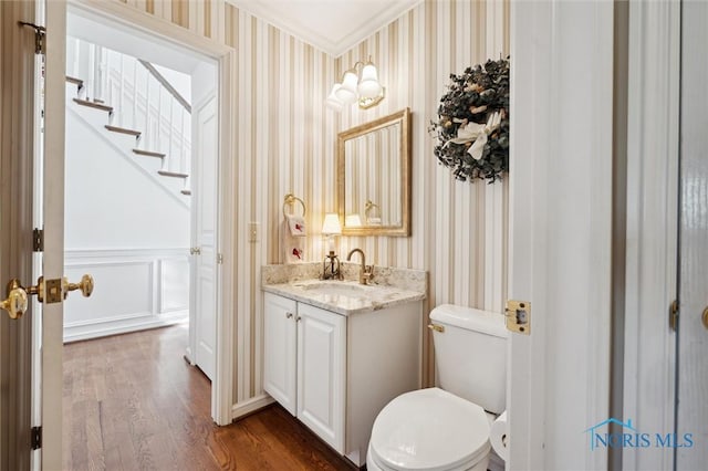half bath featuring wallpapered walls, toilet, ornamental molding, wood finished floors, and vanity