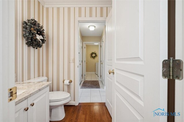 bathroom featuring vanity, toilet, baseboards, wallpapered walls, and wood finished floors