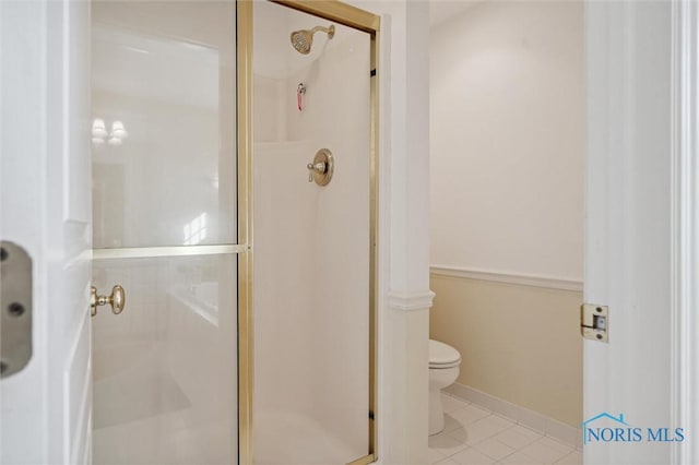 bathroom featuring toilet, tile patterned flooring, a stall shower, and baseboards