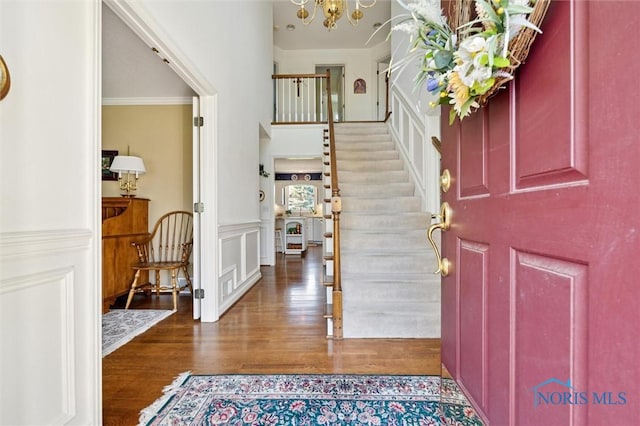 foyer featuring stairs, a towering ceiling, wood finished floors, a notable chandelier, and wainscoting