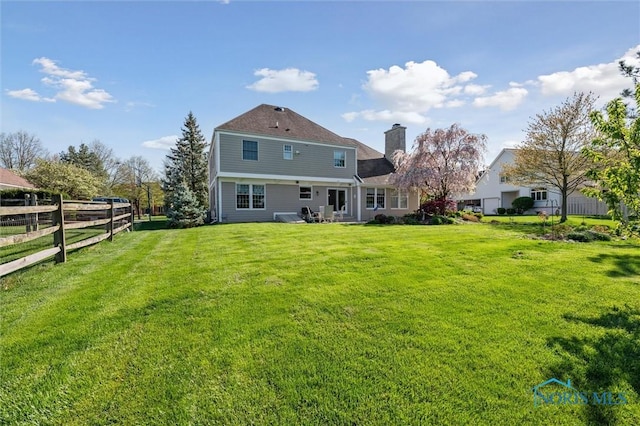 rear view of house with a lawn, a chimney, and fence
