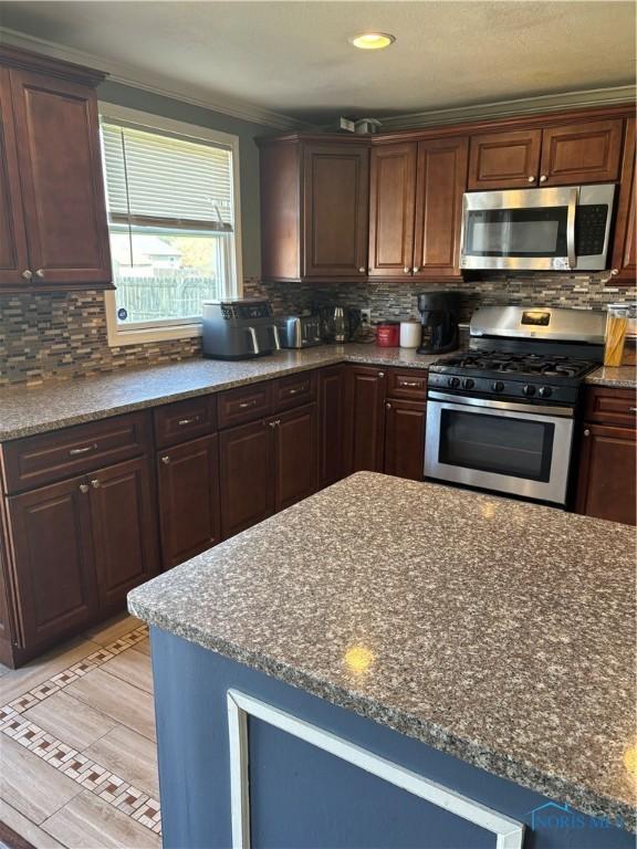 kitchen with appliances with stainless steel finishes, light tile patterned floors, tasteful backsplash, and ornamental molding