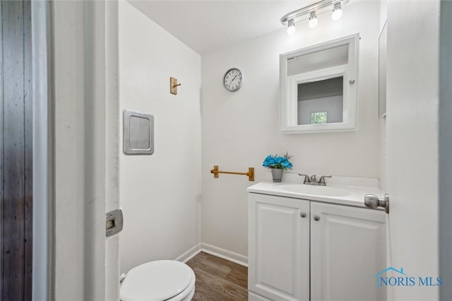 bathroom featuring toilet, baseboards, wood finished floors, and vanity