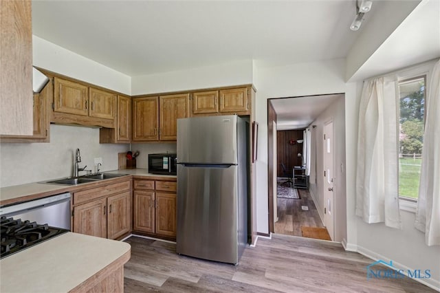 kitchen with freestanding refrigerator, black microwave, light wood-style floors, light countertops, and a sink