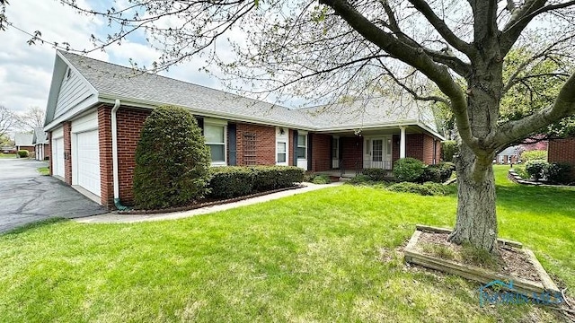 ranch-style home featuring a front yard, driveway, a shingled roof, and brick siding