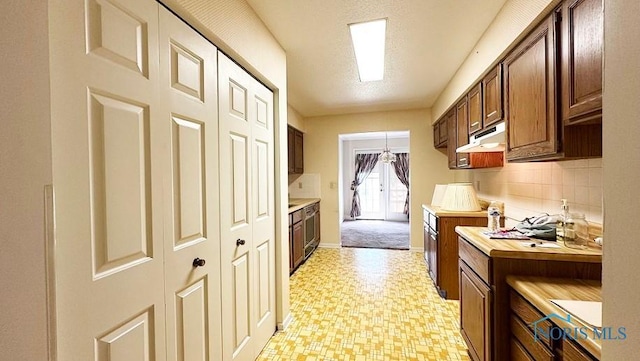 kitchen with light floors, backsplash, under cabinet range hood, and baseboards