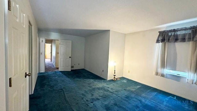 spare room featuring dark colored carpet and baseboards