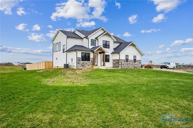 view of front of house with fence, central AC unit, stone siding, and a front lawn