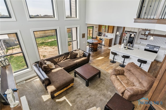 living area featuring visible vents, light wood finished floors, and a towering ceiling