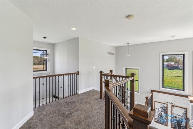 hall featuring a chandelier, carpet, baseboards, an upstairs landing, and visible vents