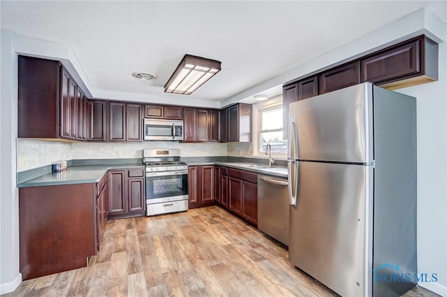kitchen with dark countertops, a sink, stainless steel appliances, light wood-type flooring, and visible vents