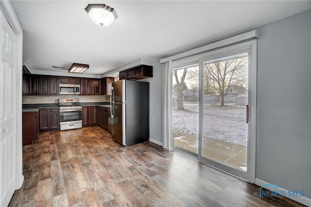 kitchen featuring dark brown cabinetry, dark countertops, stainless steel appliances, baseboards, and dark wood-type flooring