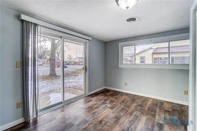 empty room with baseboards, visible vents, dark wood-style floors, and a wealth of natural light