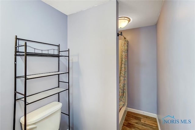 bathroom with baseboards, wood finished floors, toilet, and a shower with curtain