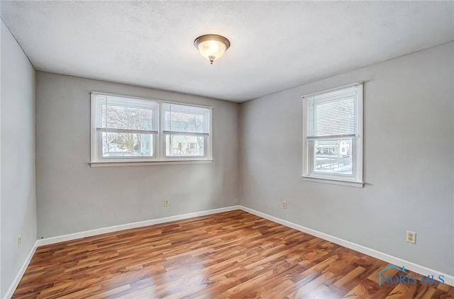 unfurnished room with plenty of natural light, baseboards, and wood finished floors