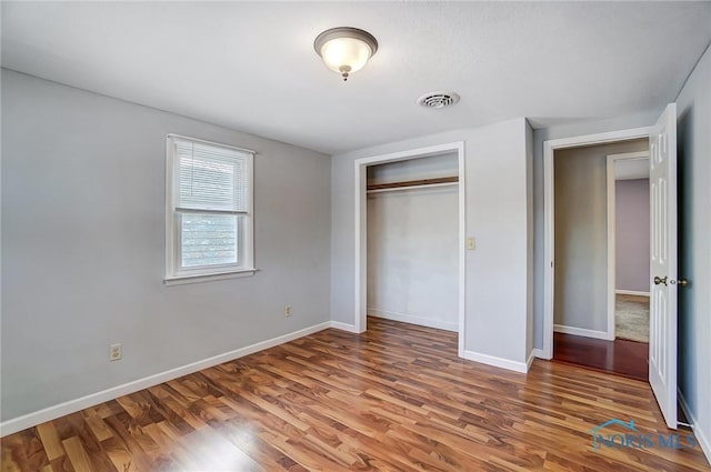 unfurnished bedroom featuring baseboards, a closet, wood finished floors, and visible vents