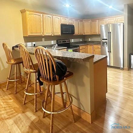 kitchen featuring light wood-style flooring, appliances with stainless steel finishes, light brown cabinets, baseboards, and a peninsula