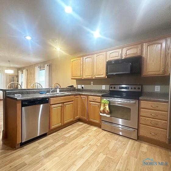 kitchen featuring light wood-style floors, appliances with stainless steel finishes, dark countertops, a sink, and a peninsula