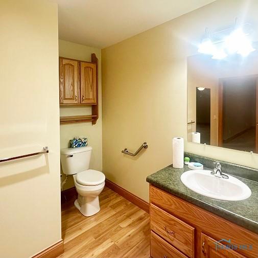 bathroom with toilet, vanity, wood finished floors, and baseboards