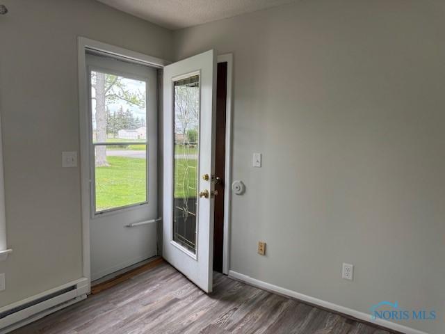 doorway to outside featuring baseboards, wood finished floors, a wealth of natural light, and a baseboard radiator