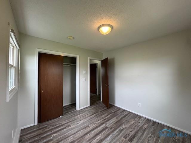 unfurnished bedroom with baseboards, wood finished floors, a textured ceiling, and a closet