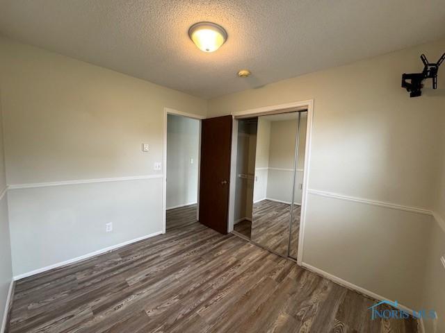 unfurnished bedroom with baseboards, wood finished floors, a textured ceiling, and a closet