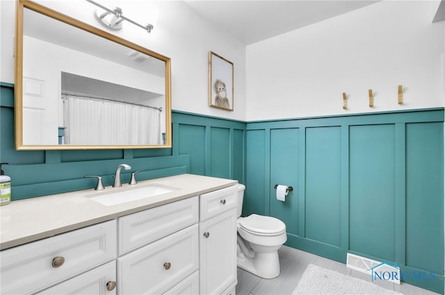 bathroom with a decorative wall, a wainscoted wall, toilet, vanity, and visible vents