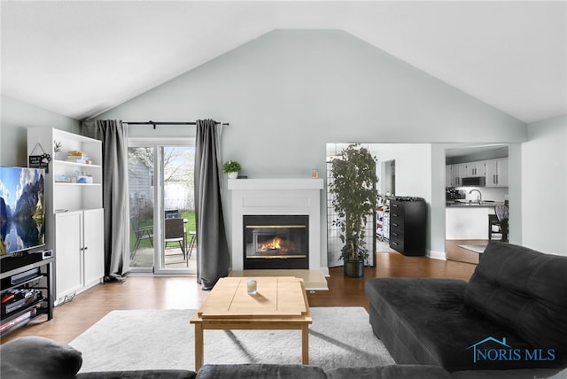 living room with high vaulted ceiling, wood finished floors, and a glass covered fireplace