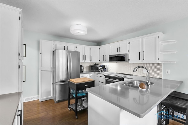 kitchen featuring white cabinetry, decorative backsplash, a sink, appliances with stainless steel finishes, and a peninsula