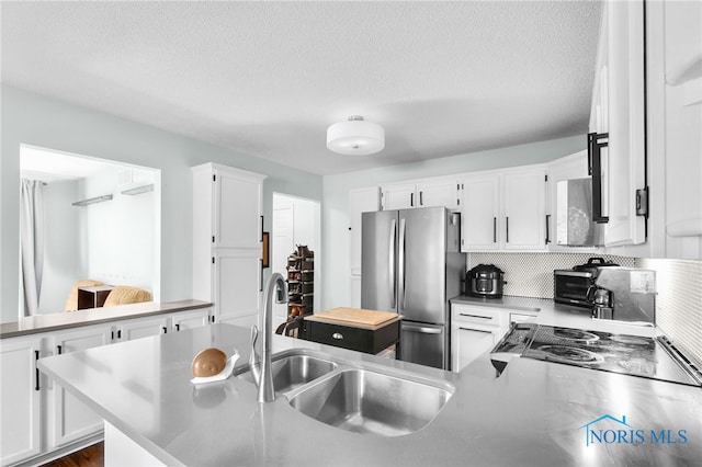 kitchen featuring white cabinets, a sink, a peninsula, and freestanding refrigerator