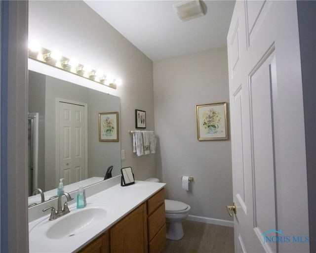 bathroom featuring toilet, baseboards, wood finished floors, and vanity