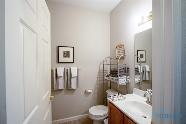 half bathroom featuring vanity, baseboards, and toilet