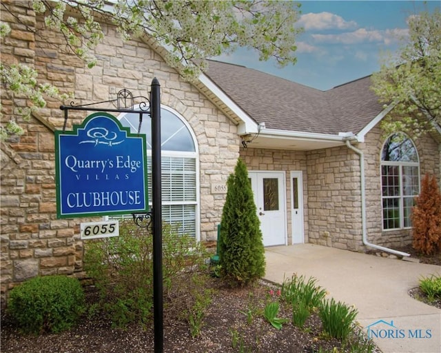 doorway to property featuring roof with shingles and stone siding
