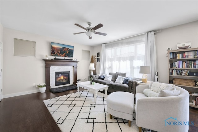 living room with baseboards, ceiling fan, wood finished floors, and a tiled fireplace