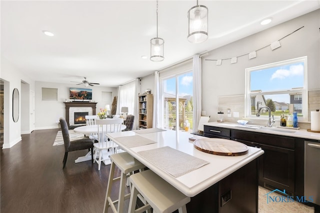 kitchen featuring a sink, a glass covered fireplace, wood finished floors, light countertops, and a ceiling fan