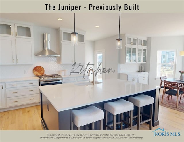 kitchen with white cabinets, light wood-style flooring, wall chimney exhaust hood, and gas range