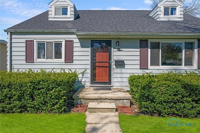 entrance to property with a shingled roof and a yard