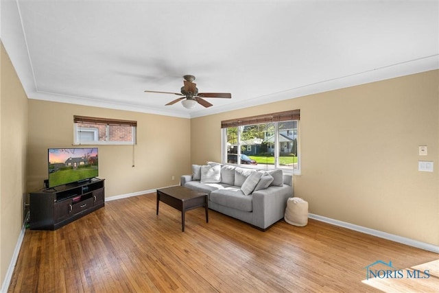 living room with hardwood / wood-style flooring, crown molding, a ceiling fan, and baseboards