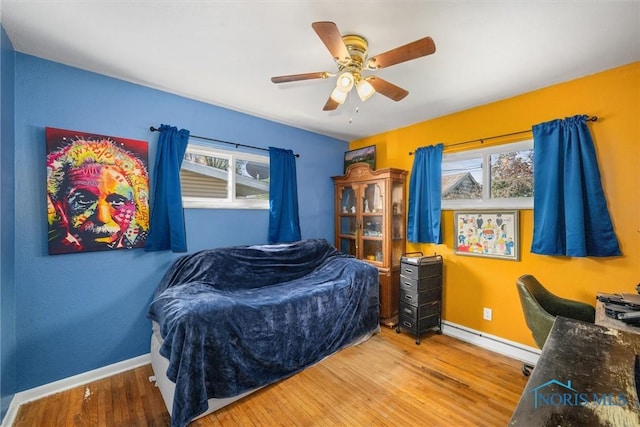 bedroom with baseboard heating, baseboards, wood finished floors, and a ceiling fan