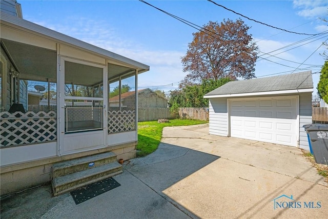 exterior space featuring a sunroom, an outdoor structure, a detached garage, driveway, and fence